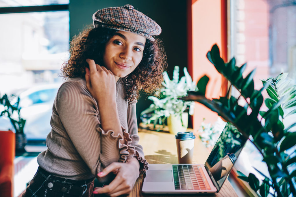 millennial female in stylish hat posing during laptop remote working